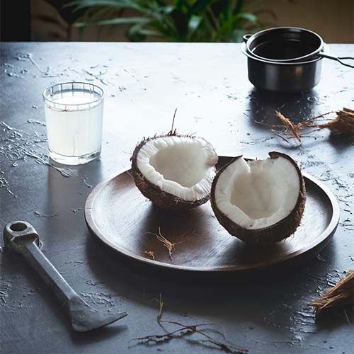 An opened coconut sits next to a jar of oil and some utensils