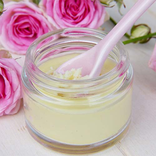 An opened jar of shea butter sits on a table with some flowers around it